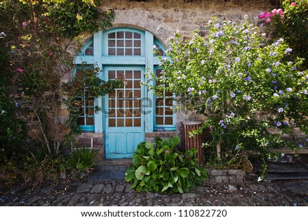 view of a painterly Breton cottage with climbing roses and hibiscus