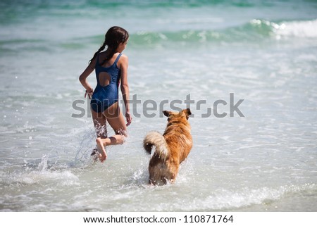 pretty girl and her dog running on the water at the beach