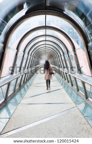 business woman in motion blur walking over a pedestrian bridge with glass dome in La Defense, Paris
