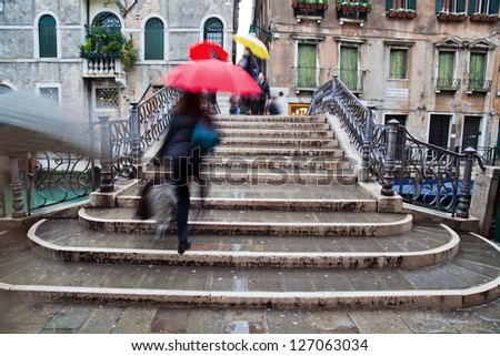 picture of a rainy day in Venice with an old bridge and crossing people with umbrellas