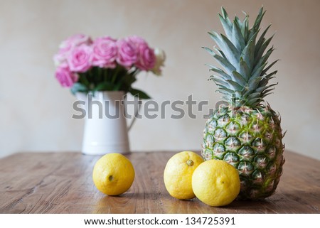 still life picture with pineapple, three lemons and a vase with pink roses