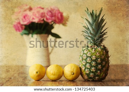 vintage style still life picture with pineapple, lemons and a vase with pink roses