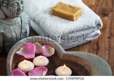 stone heart with water rose petals and floating candles and buddha head and towels with soap in the background