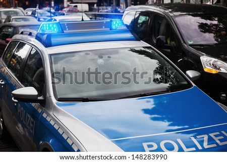German police car standing with blue lights on a city street with passing cars
