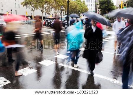 people with umbrellas in motion blur crossing the wet city street