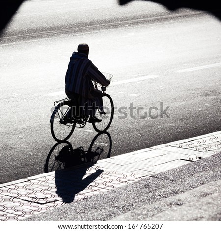 backlit silhouette of an arabian man with a bicycle on a city street