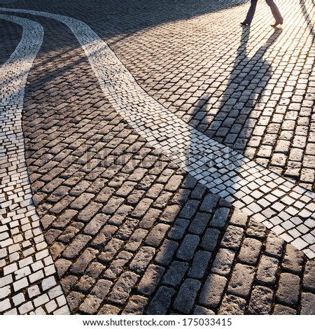 cobblestone square with white wavy stripes and a long shadow of a walking person