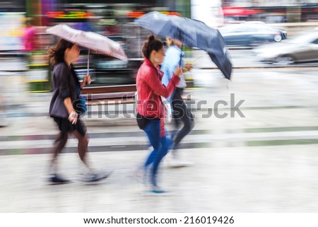 women with rain umbrellas walking in the rainy city in motion blur