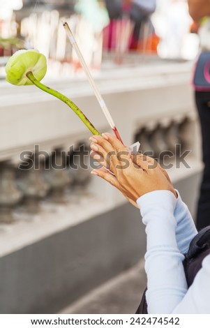 Buddhist woman prays with incense sticks and a flower between her hands