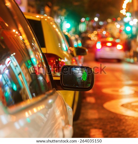 parked car on a city road at night with focus on the rear mirror and blurred background with colorful lights