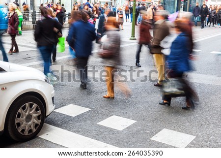 pedestrians in motion blur crossing a city street while car is waiting