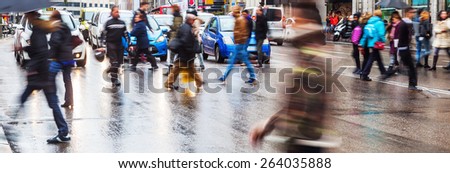 panoramic photo of a crowd of people crossing a wet street in the rainy city