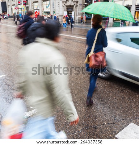people in motion blur crossing a city street on a rainy day