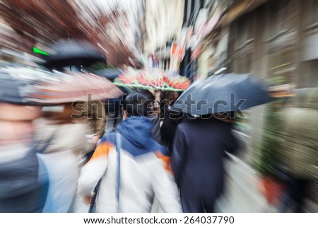 picture with camera made zoom effect of people with umbrellas in the rainy city