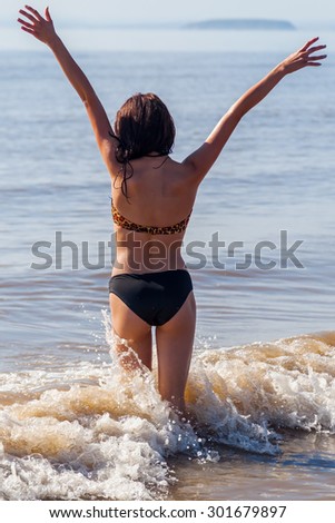 young girl with raised hands standing in the water of the sea at a beach in Somerset, England