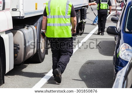 security personnel walking with a detection dog along lorries at a ferry port gate