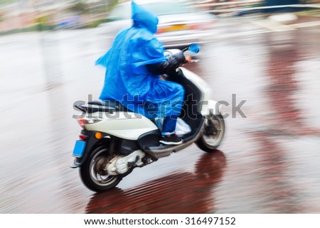 scooter rider in a blue cape on the move in the rainy city in motion blur