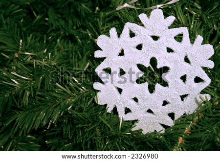 Close-up of a pale blue snowflake on a background of artificial pine foliage.