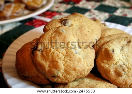 Chocolate chip cookies on a white plate with a Christmas quilt background.