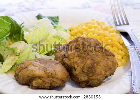 A dinner of three crab cakes with tossed green salad and whole kernel corn.