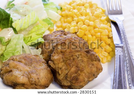 A dinner of three crab cakes with tossed green salad and whole kernel corn.