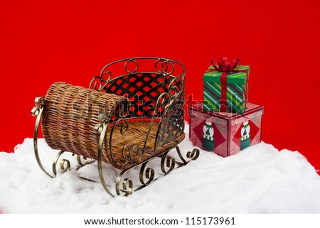 Shot of a wicker sleigh on fax snow with presents laying in the snow outside of of it.