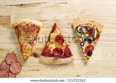 Top view of three baked pizza pie with slices of ham over wooden surface