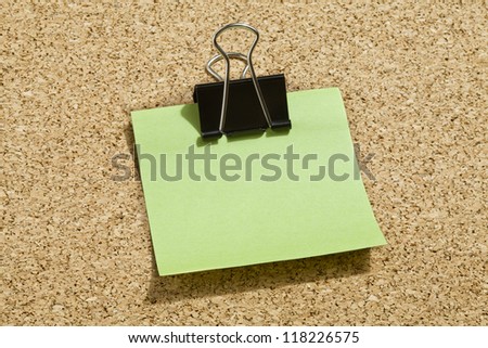 Green memo note with black binder clip over a cork board background