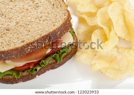 Close up image of ham sandwich with potato chips against white background