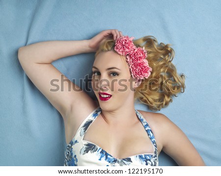 Portrait shot of a sexy female model wearing pink flower and lying on blue surface. Model: Amanda Wynne