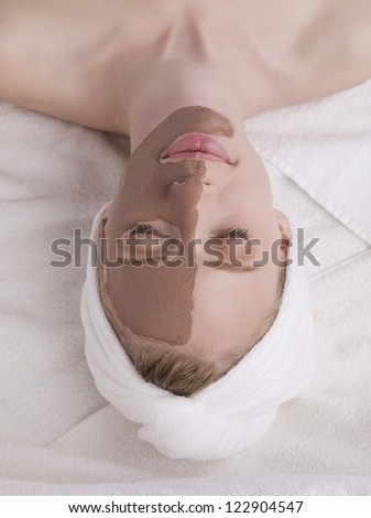 Upside down image of a woman with mud mask on the half of her face