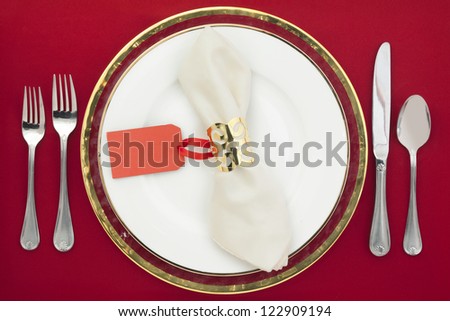 Horizontal image of dinner table with utensils and empty tag on a red background