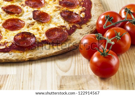 A close-up cropped image of a pan pizza on the table with a fresh tomato on the side