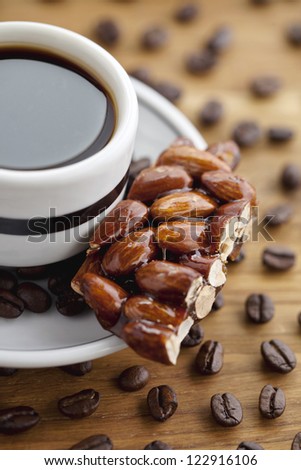 Close-up cropped shot of a black coffee cup with saucer, almond confection and coffee beans.