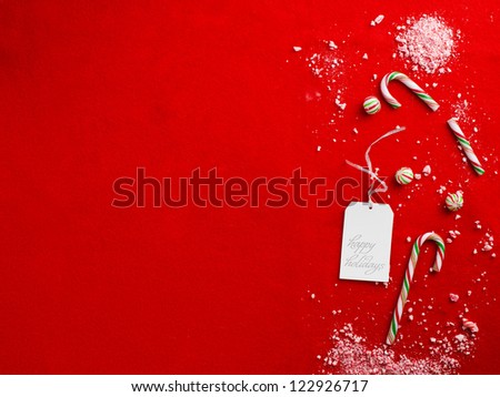 Close-up top view of broken candy canes and happy holidays tag over plain red background.
