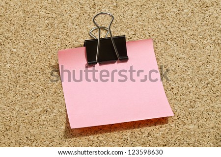 Pink memo note with black binder clip over a cork board background