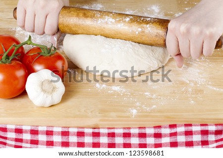 Image of a hand holding a rolling pin to knead the pizza dough on the wooden table
