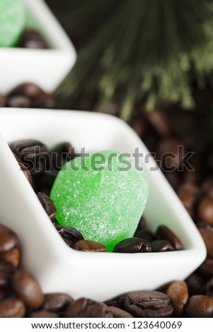 A close-up portrait of a green jelly candy and a coffee bean on a small white bowl