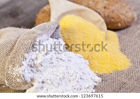 Spilled  burlap sack of wheat and maize flour with a wooden ladle and bread at the background