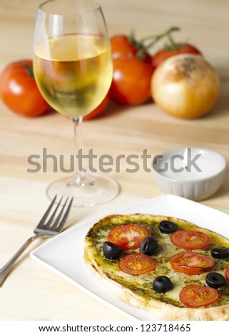 Pizza with glass of wine and tomatoes in background
