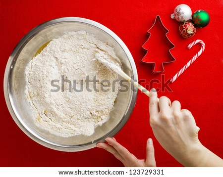 Image of someone mixing flour in chocolate syrup with spatula with cookie cutter and Christmas baubles over red background.