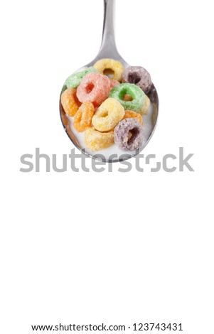 Close-up shot of a spoon with colorful cereal rings and milk against white background.