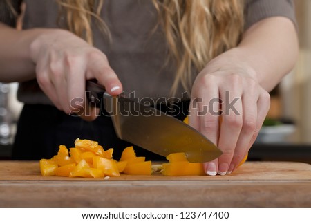 Close up image of chopping orange bell pepper on the wooden chopping board
