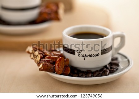 Black coffee with coffee beans and almond bar on in a white saucer