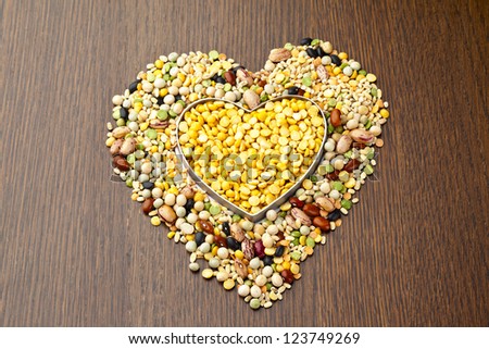 Close-up shot of food grains assorted in heart shape on wooden table.