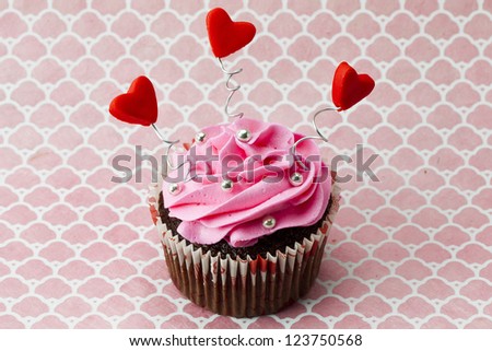 Close-up high angle view of strawberry cupcake with heart shapes and beads sticking out of it.