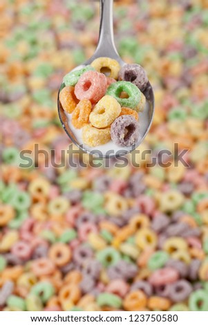 Close-up image of a spoon with colorful cereals and milk with blurred cereals on the background