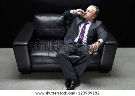 View of a mafia in full suit sitting on couch and smoking cigar