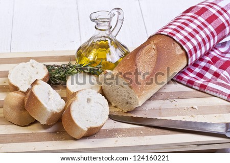 Sliced baguette bread, olive oil and bread knife on top of a wooden chopping board