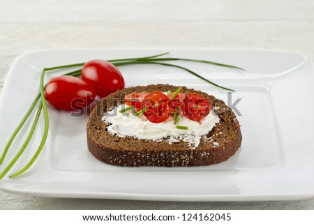 Close up image of slice of pumpernickel bread with cream cheese and tomato slices on white plate